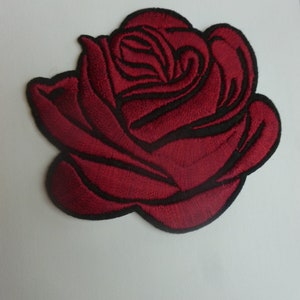May include: A red embroidered rose patch. The rose is a single bloom with a dark red color and black stitching.