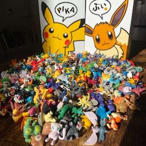 May include: A large collection of colorful Pokemon figurines, including Pikachu and Eevee, are displayed in front of two boxes with the Japanese characters for "Pika" and "Eevee" on them.