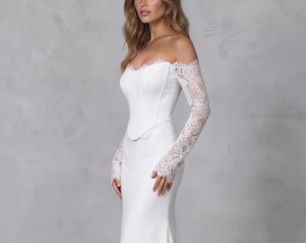 May include: A floor-length white gown featuring an off-the-shoulder corset bodice with structured seams and long, sheer lace sleeves. The skirt is fitted through the hips and flares slightly toward the floor, creating a streamlined silhouette.