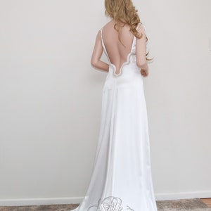 May include: A white satin wedding dress with a low back and a lace trim. The dress has a flowing skirt and a simple, elegant design.