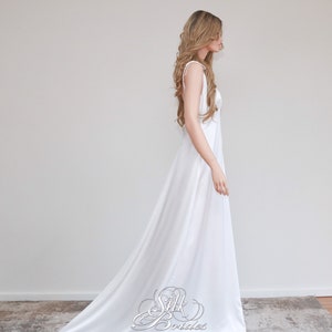 May include: A white sleeveless maxi dress with a simple design and a long train. The dress is made of a smooth, flowing fabric.