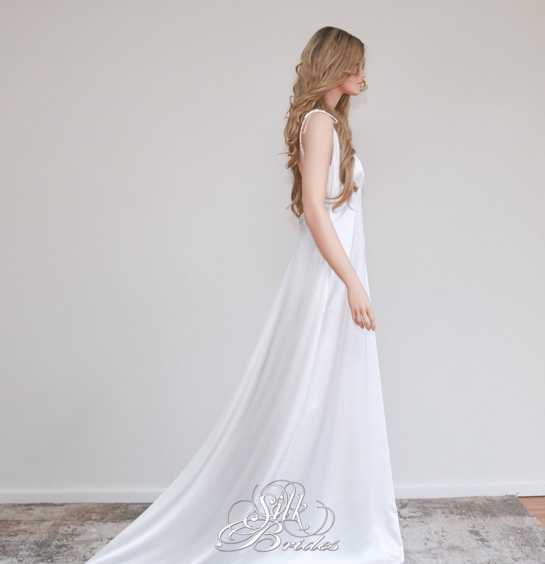 May include: A white sleeveless maxi dress with a simple design and a long train. The dress is made of a smooth, flowing fabric.