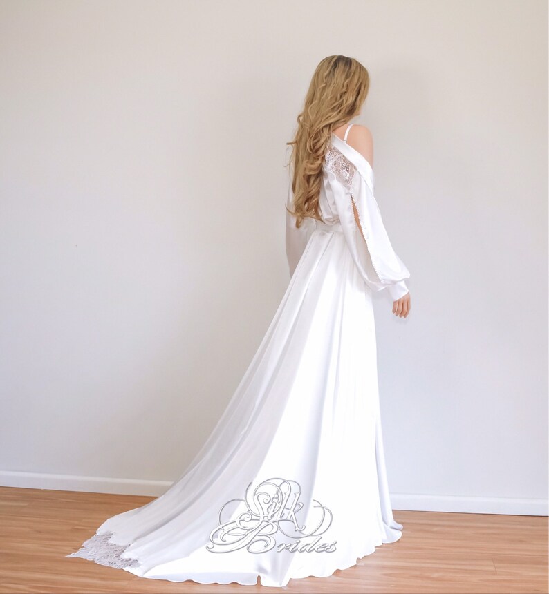 May include: A white satin bridal robe with a lace overlay and long sleeves. The robe has a flowing train and is perfect for a wedding day.