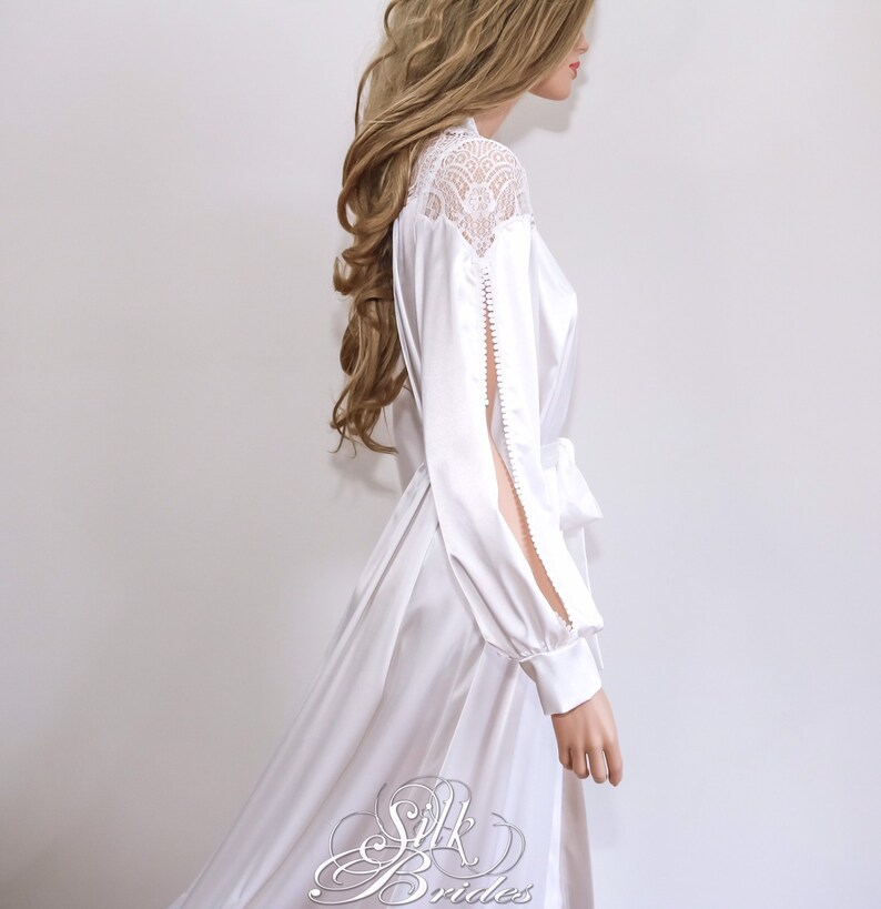 May include: White satin robe with long sleeves and a lace overlay on the shoulders. The robe has a sash tie at the waist and a slit on each sleeve.