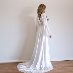 May include: A white satin robe with long sleeves and a lace trim. The robe has a tie belt and a long train.