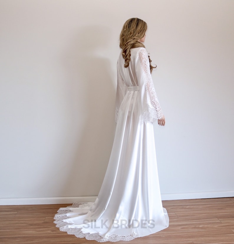 May include: A white satin robe with long sleeves and a lace trim. The robe has a tie belt and a long train.