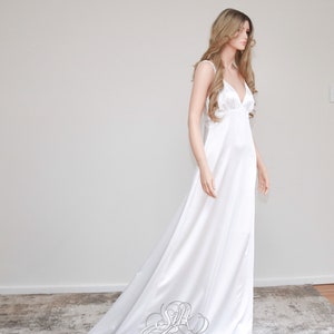 May include: A white silk wedding dress with a simple, elegant design. The dress has a V-neckline and spaghetti straps. The skirt is flowing and has a slight train.