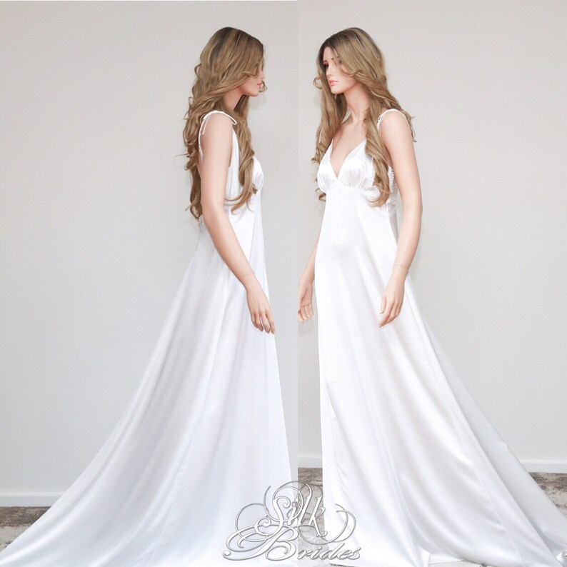 May include: A white satin slip dress with a V-neckline and thin straps. The dress has a long flowing skirt and is shown on a mannequin.