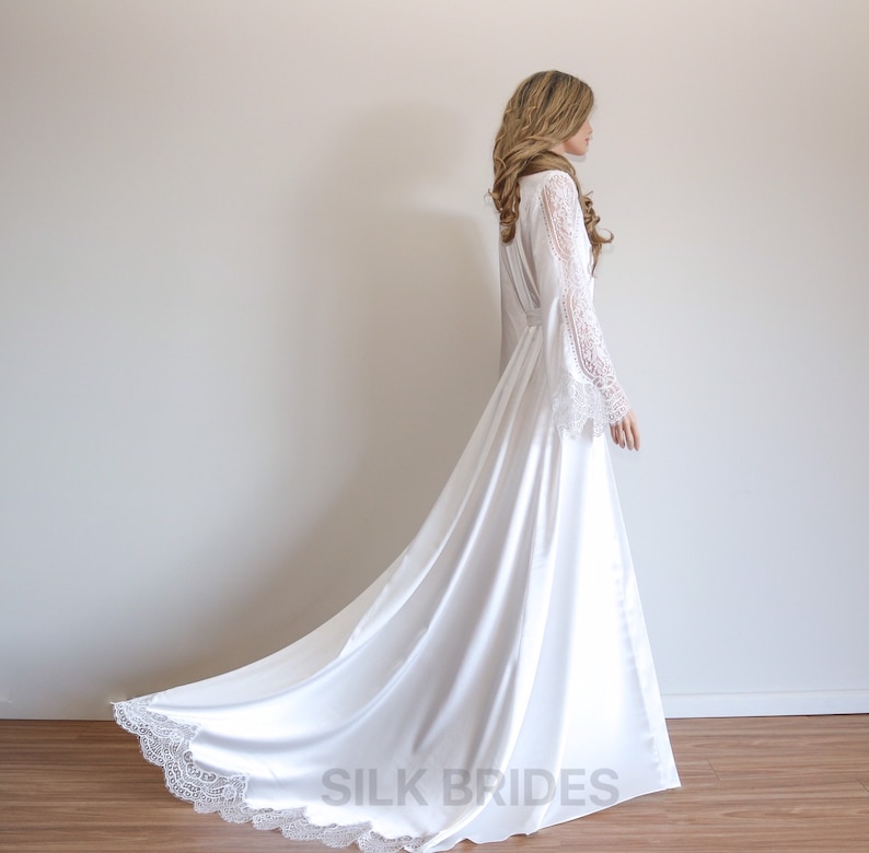 May include: A white satin robe with long, lace sleeves and a lace trim. The robe has a long train and is tied at the waist with a sash. The text "SILK BRIDES" is printed on the bottom of the robe.