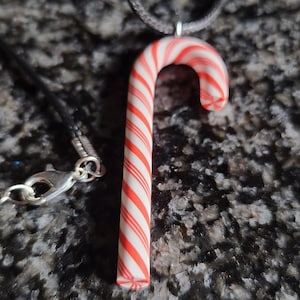 May include: A red and white candy cane pendant on a black cord necklace. The candy cane is a traditional Christmas decoration.