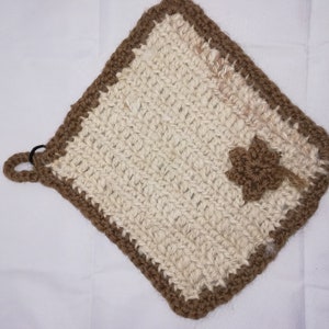 Könnte beinhalten: Ein brauner und weißer gehäkelter Topflappen mit Blumenmuster. Der Topflappen hat eine Schlaufe zum Aufhängen.