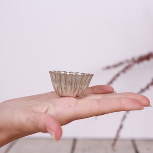 May include: A small, silver, fluted, metal baking dish, similar to a tart pan, is held in a person's hand.