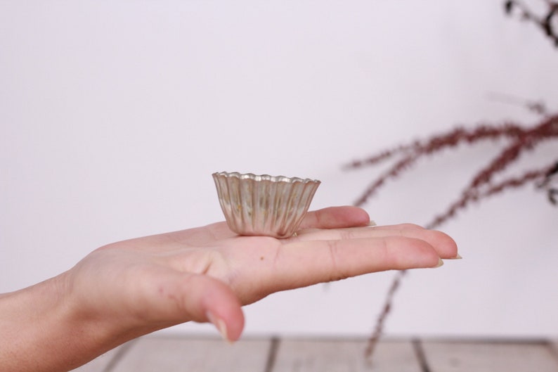 May include: A small, silver, fluted, metal baking dish, similar to a tart pan, is held in a person's hand.