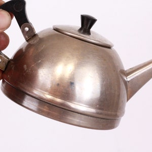 May include: A silver teapot with a black plastic handle and lid. The teapot has a rounded body and a spout on the side.