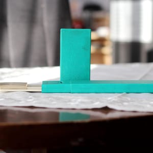 May include: A teal blue rectangular box with a smaller teal blue rectangular piece attached to the top. The box is sitting on a white surface.