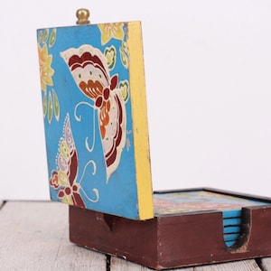 May include: A wooden box with a hinged lid, decorated with a colorful butterfly pattern. The lid is open, revealing a stack of coasters with a similar butterfly design.