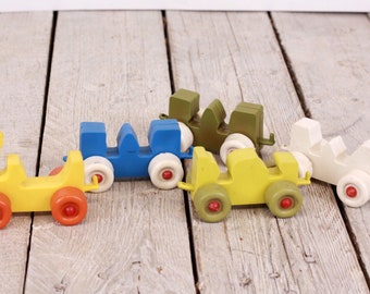 May include: Five vintage toy cars in a train formation. The cars are yellow, blue, green, white, and yellow. The cars have red wheels and are made of plastic.