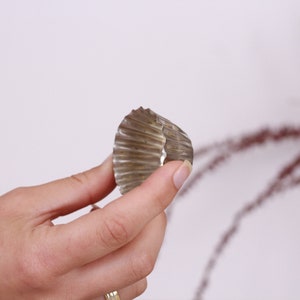 May include: A silver cupcake liner, also known as a muffin cup, is held in a person's hand. The liner is made of metal and has a fluted edge.