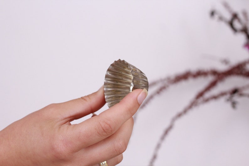 May include: A silver cupcake liner, also known as a muffin cup, is held in a person's hand. The liner is made of metal and has a fluted edge.