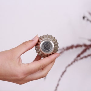 May include: A silver metal cupcake mold with a fluted edge. The mold is being held in a hand.