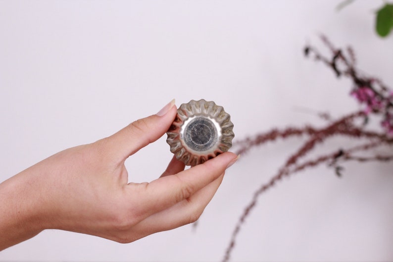 May include: A silver metal cupcake mold with a fluted edge. The mold is being held in a hand.