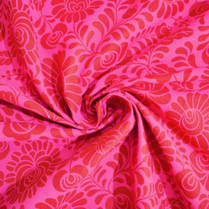 May include: Pink fabric with a red floral pattern. The fabric is folded and the pattern is visible on both sides.