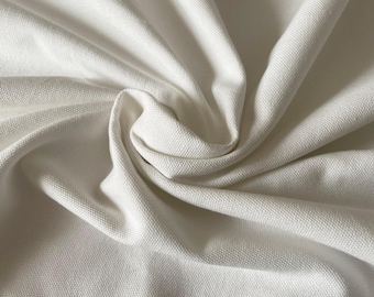 May include: Close-up of a white canvas fabric with a textured surface. The fabric is folded and draped, showing its soft and smooth texture.