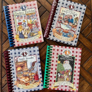 May include: Four spiral-bound Gooseberry Patch cookbooks featuring illustrated covers. Titles include Hometown Favorites, In the Kitchen with Family & Friends, Family Favorites, and Old-Fashioned Country Christmas, each with distinct plaid borders and colorful artwork.