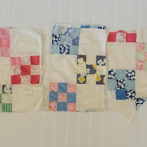 May include: Three rectangular fabric quilt blocks featuring a nine-patch pattern. Each block consists of solid white squares interspersed with smaller squares in various colors including pink, blue, yellow, green, and floral patterns.