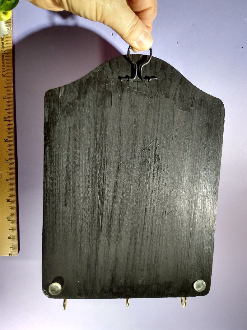 May include: Black wooden key holder with a metal hook at the top and three metal hooks at the bottom. The key holder has a distressed finish.