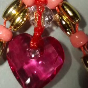 May include: A red string with pink and gold beads, a clear crystal bead, and a pink heart-shaped charm.