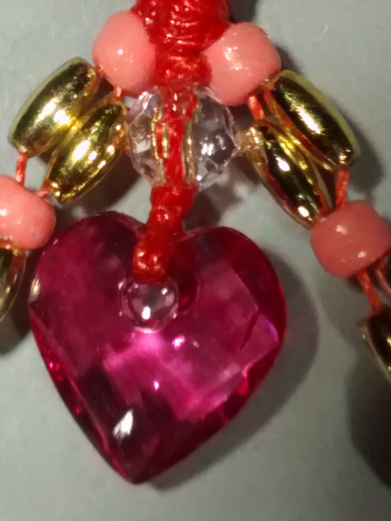 May include: A red string with pink and gold beads, a clear crystal bead, and a pink heart-shaped charm.