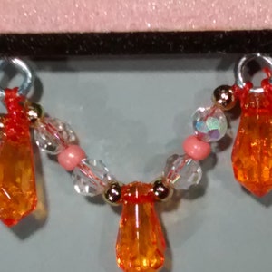 May include: A necklace featuring orange teardrop-shaped beads, clear beads, and pink beads.