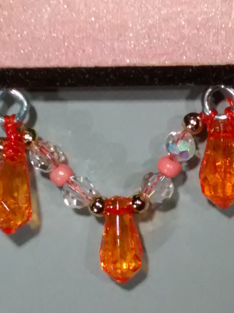 May include: A necklace featuring orange teardrop-shaped beads, clear beads, and pink beads.