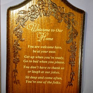 May include: A wooden sign with a carved floral design and the text "Welcome to Our Home". The sign has a poem about being welcome and comfortable. The sign has three key hooks.