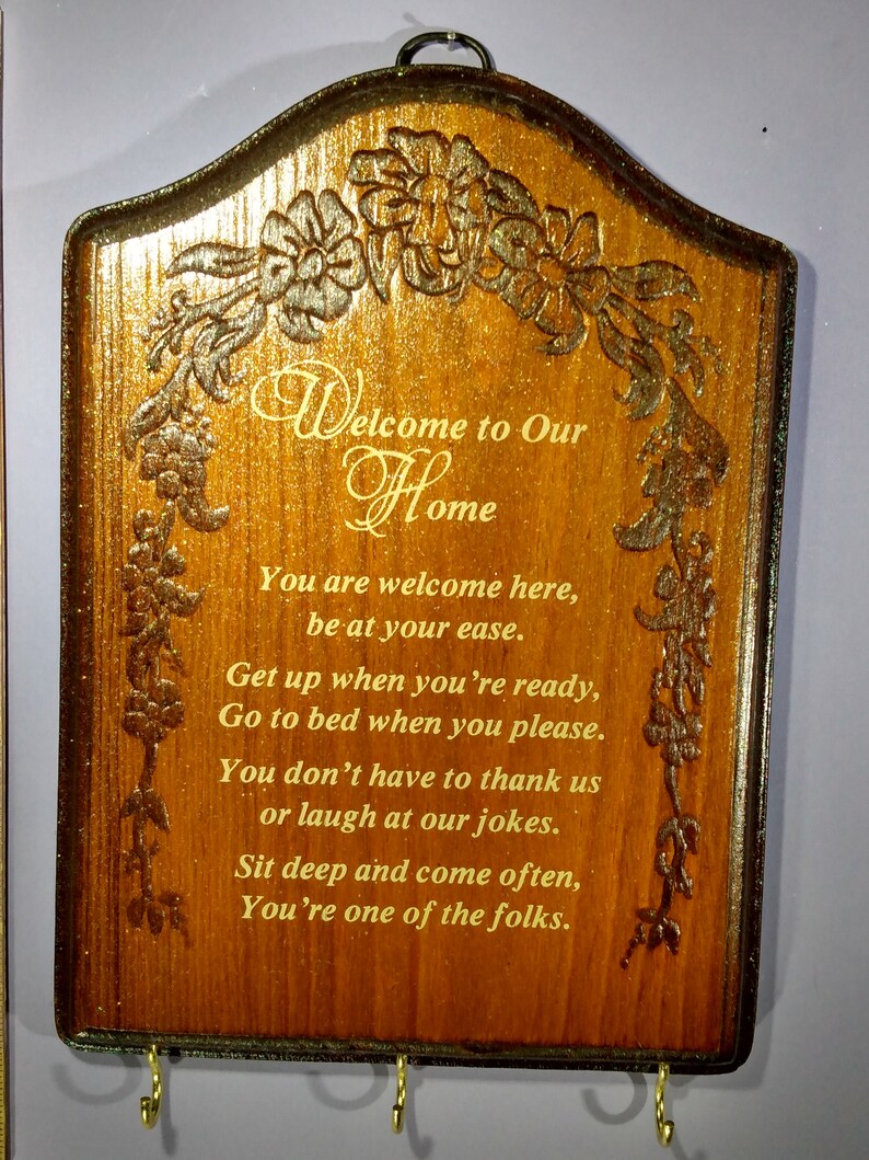 May include: A wooden sign with a carved floral design and the text "Welcome to Our Home". The sign has a poem about being welcome and comfortable. The sign has three key hooks.