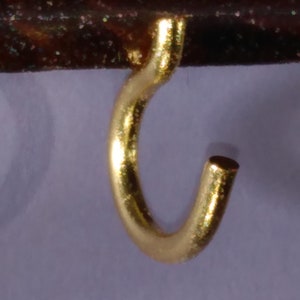 May include: A gold-colored metal hook with a rounded shape. The hook is designed to hang items on a surface.