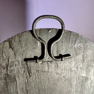 May include: A round wooden wall decor with a black finish and a metal handle on the back. The handle is shaped like a loop and has two small metal tabs on either side.