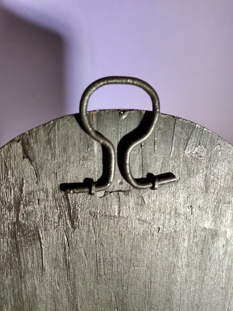 May include: A round wooden wall decor with a black finish and a metal handle on the back. The handle is shaped like a loop and has two small metal tabs on either side.