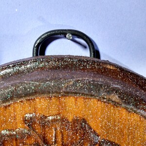 May include: A wooden round ornament with a glittery brown finish and a carved floral design. The ornament has a black metal hook on the top.