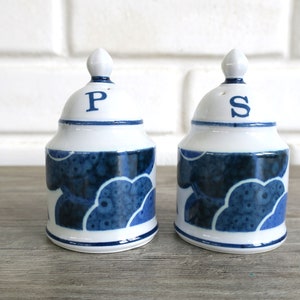 May include: A set of blue and white ceramic salt and pepper shakers with a cloud pattern. The shakers have a dome-shaped lid with the letters "P" and "S" on top.