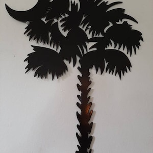 May include: Black metal silhouette of a palm tree with a crescent moon, a popular symbol of South Carolina.