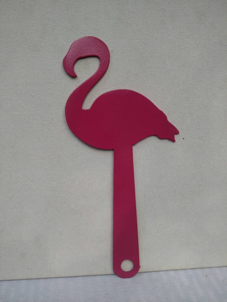 K&ouml;nnte beinhalten: Eine rosafarbene Metall-Flamingo-Silhouette mit einem langen, d&uuml;nnen Stiel. Der Flamingo steht auf einer wei&szlig;en Oberfl&auml;che.