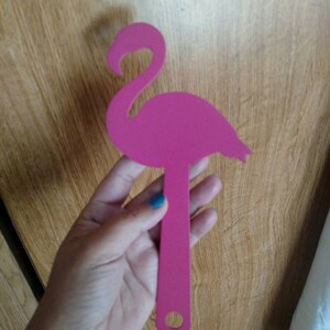 K&ouml;nnte beinhalten: Rosafarbener Flamingo aus Plastik mit einem Loch am unteren Ende des Stiels. Die Aussparung wird in einer Hand gehalten.