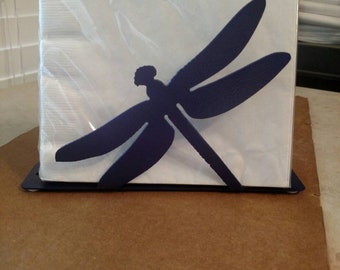 May include: A dark blue metal dragonfly napkin holder. The holder is designed to hold a stack of paper napkins.