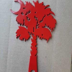 May include: A red metal palm tree cutout with a crescent moon at the top. The palm tree is a popular symbol of the state of South Carolina.