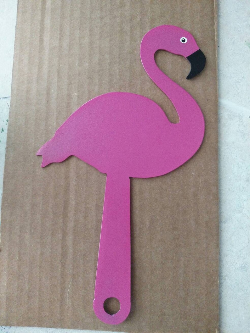 K&ouml;nnte beinhalten: Rosafarbener Metall-Flamingo-Ausschnitt mit schwarzem Auge und Schnabel. Der Flamingo steht auf einer braunen Pappe.