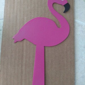 K&ouml;nnte beinhalten: Pinkfarbene Metall-Flamingo-Silhouette mit schwarzem Schnabel und Auge. Der Flamingo ist an einer Metallstange mit einem Loch am Boden befestigt.