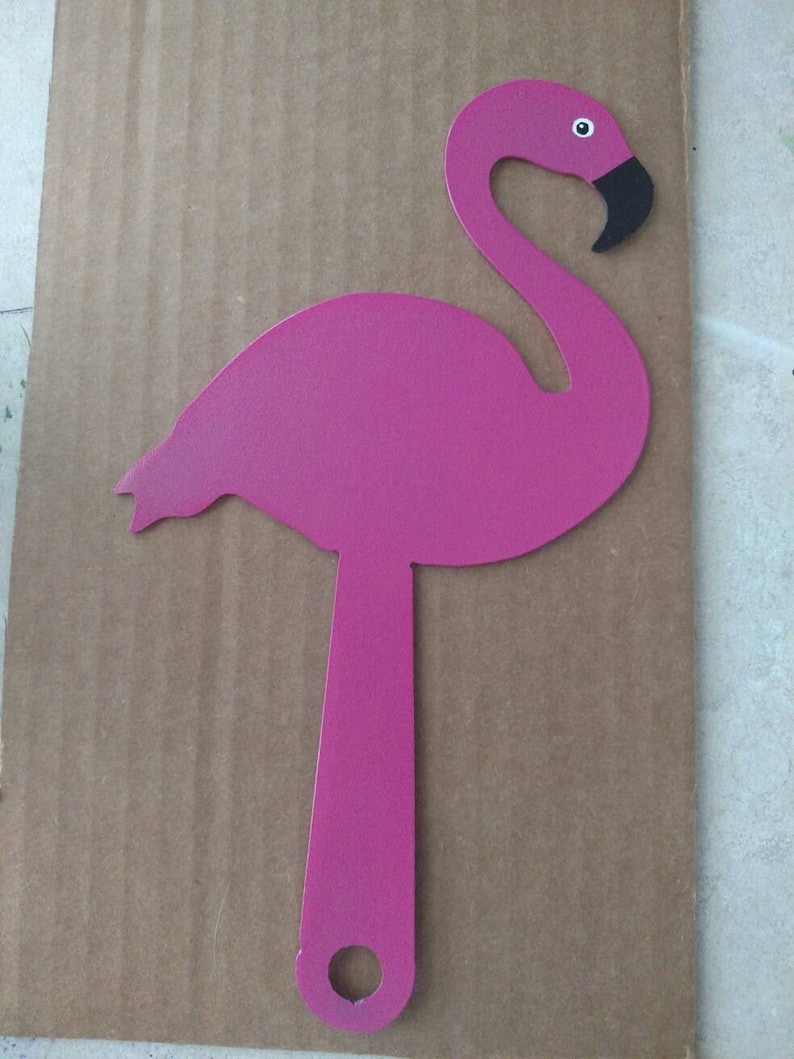 K&ouml;nnte beinhalten: Pinkfarbene Metall-Flamingo-Silhouette mit schwarzem Schnabel und Auge. Der Flamingo ist an einer Metallstange mit einem Loch am Boden befestigt.