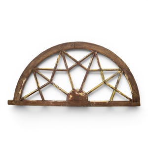 May include: A semi-circular wooden window frame featuring a star-shaped muntin pattern. The wood has a weathered brown finish with visible patches of chipped yellow paint on the interior spokes and a straight horizontal base beam.